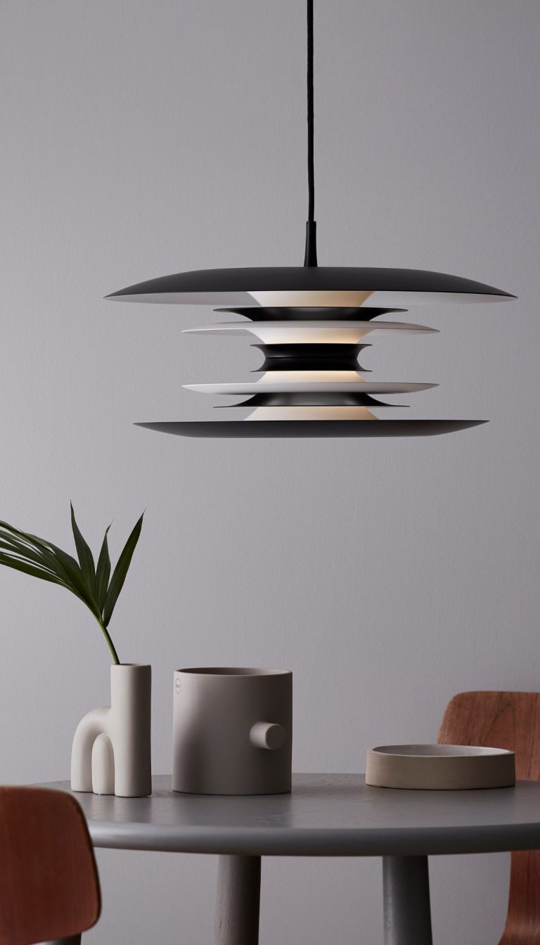 Moderner Pendelleuchte über einem Tisch mit grauen und roten Elementen und einer Pflanze.