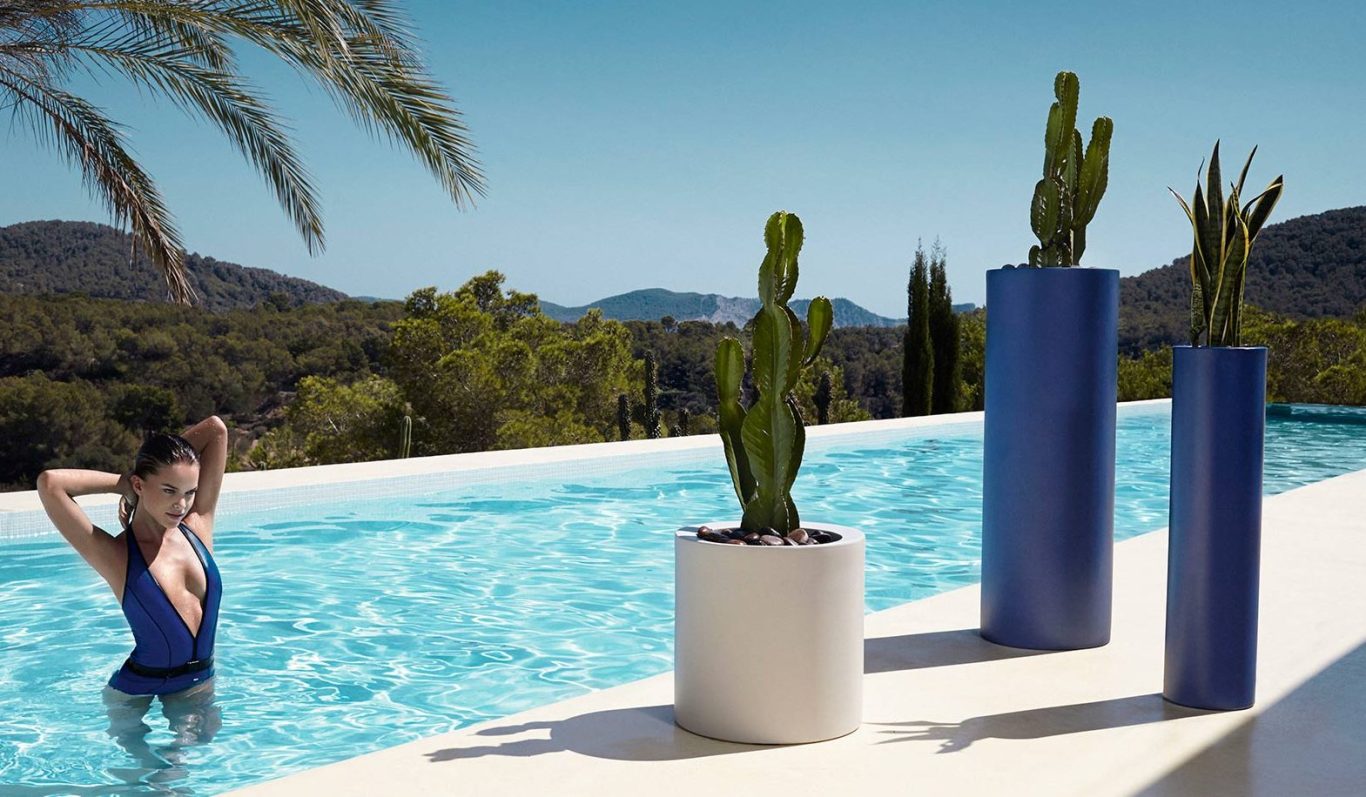 Drei moderne Pflanzengefäße mit Kaktussen neben einem Pool in sonniger Umgebung.