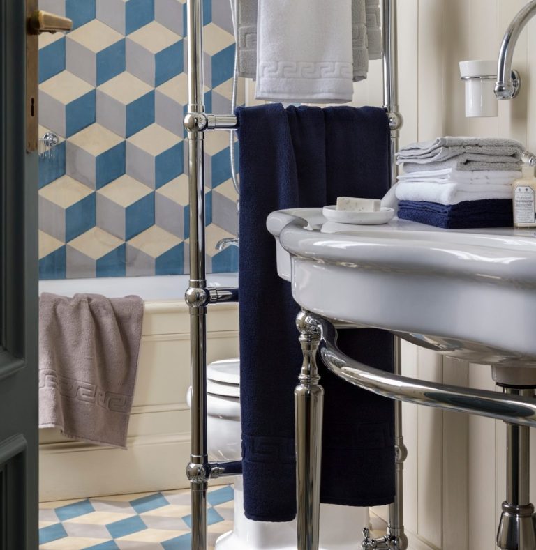 Badezimmer mit geweißter Wand, blauen Fliesen und Handtüchern an einem Ständer.