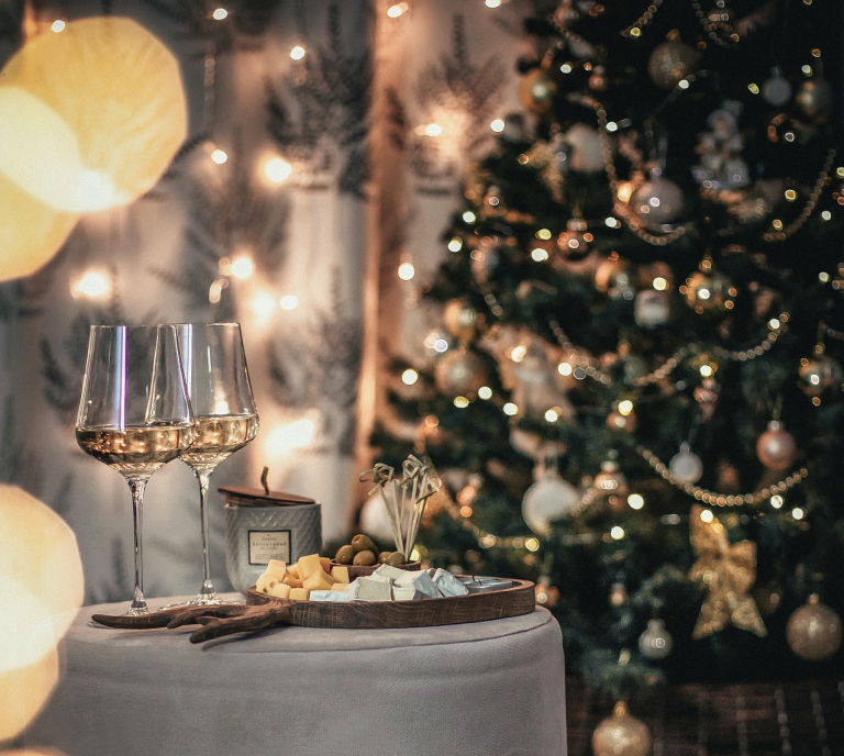Weihnachtlicher Tisch mit Gläsern, Snacks und festlich geschmücktem Baum im Hintergrund.