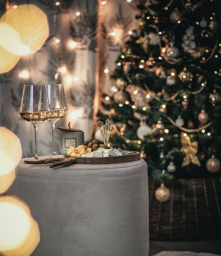 Weihnachtlicher Tisch mit Gläsern, Snacks und festlich geschmücktem Baum im Hintergrund.