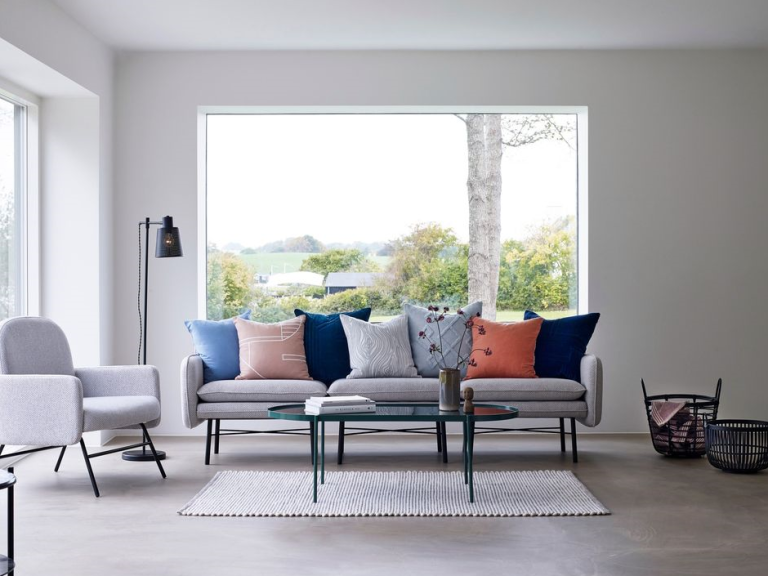 Heller Wohnraum mit Sofa, Kissen in verschiedenen Farben und großem Fenster.