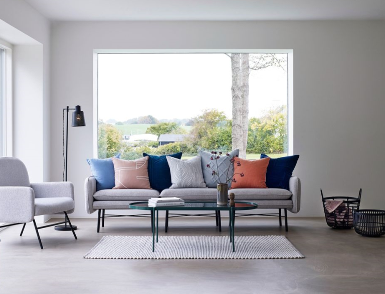 Heller Wohnraum mit Sofa, Kissen in verschiedenen Farben und großem Fenster.