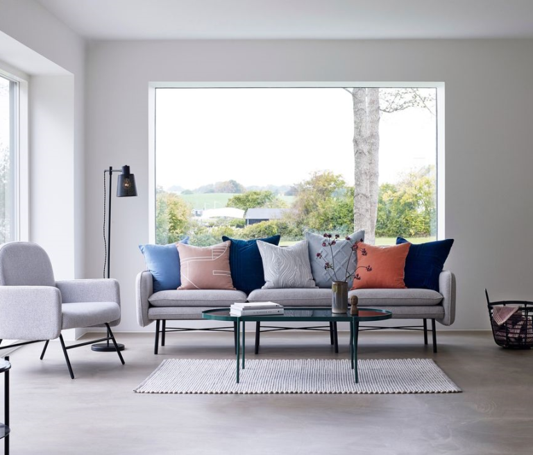 Heller Wohnraum mit Sofa, Kissen in verschiedenen Farben und großem Fenster.