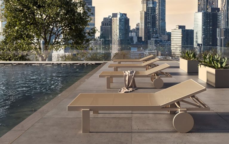 Sonnenliegen am Rand eines Pools mit Stadtlandschaft im Hintergrund.