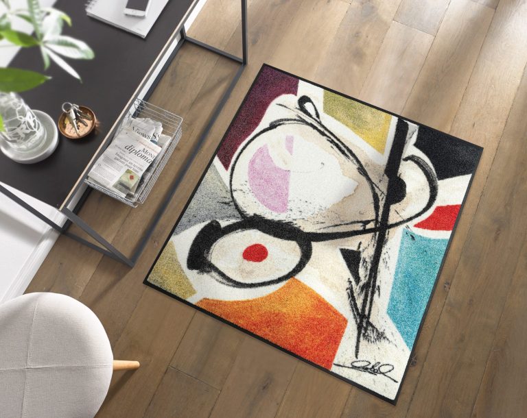 Bunter Teppich mit abstrakten Formen in Schwarz, Rot, Gelb und Blau auf einem Holzboden.