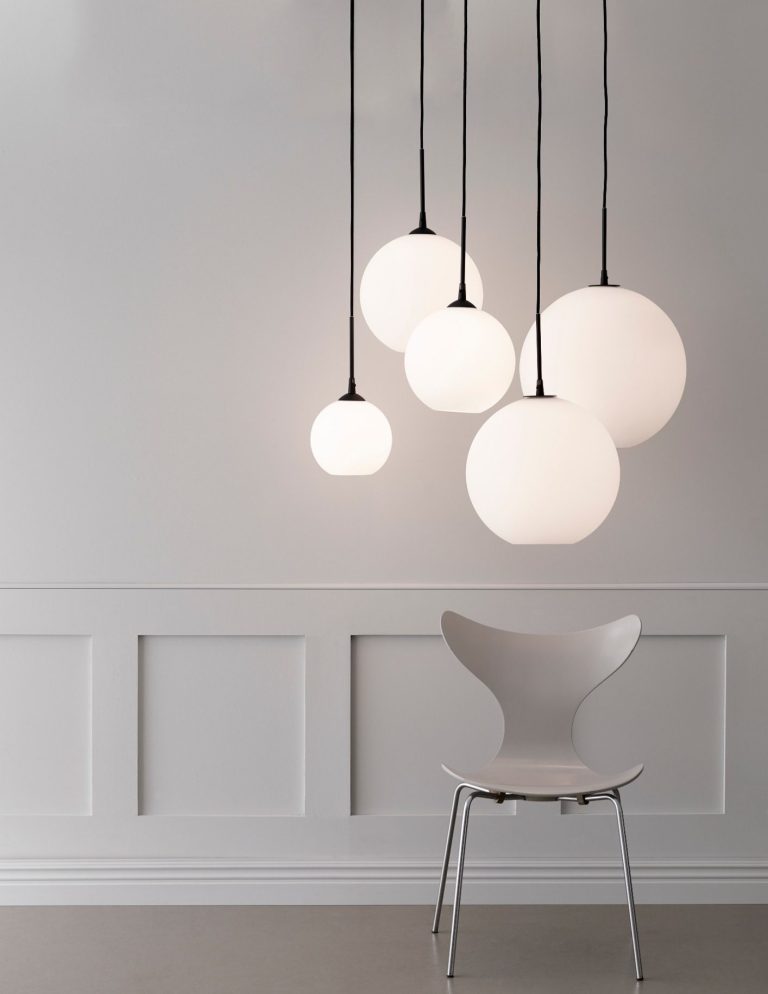Fünf hängende, runde Lampen über einem modernen, weißen Stuhl in einem minimalistischen Raum.