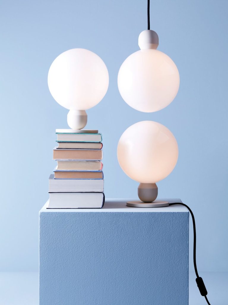 Drei große, runde Lampen auf einem Stapel Bücher vor einer blauen Wand.
