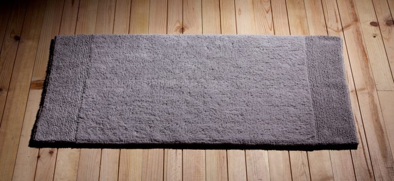 Grau gefärbter Teppich auf einem Holzfußboden, rechteckige Form.