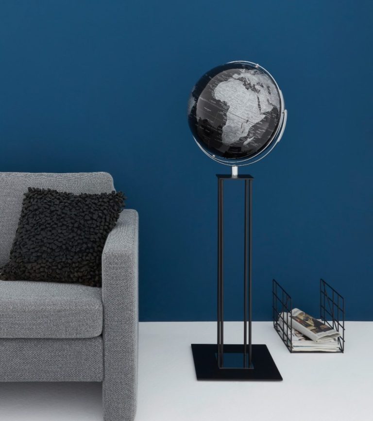 Ein stilvoller Globus auf einem Standfuß, vor einer blauen Wand, mit einem Magazinhalter daneben.