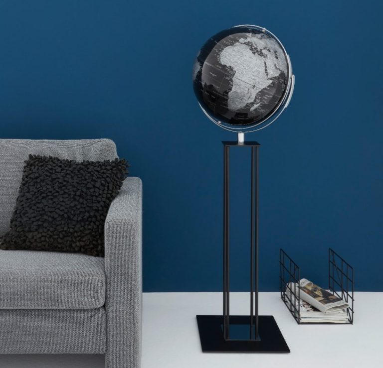 Ein stilvoller Globus auf einem Standfuß, vor einer blauen Wand, mit einem Magazinhalter daneben.