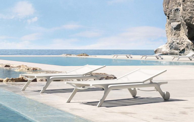 Zwei weiße Liegen am Rand eines Pools mit Blick auf das Meer und den Himmel.