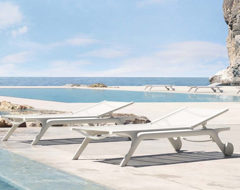 Zwei weiße Liegen am Rand eines Pools mit Blick auf das Meer und den Himmel.