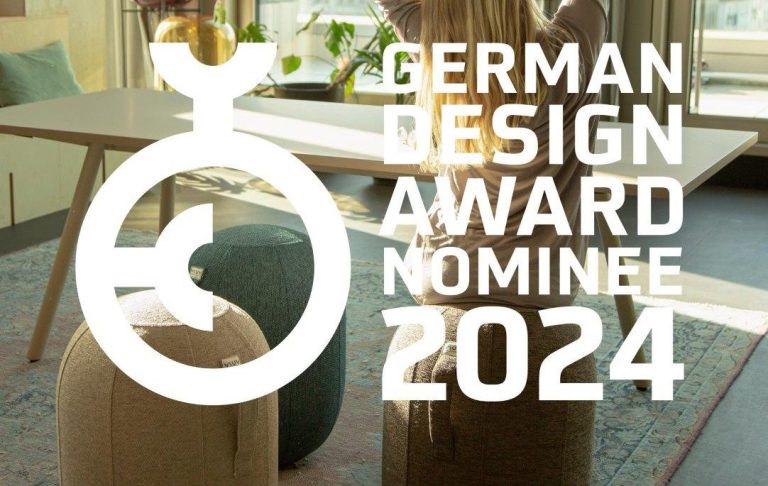 Frau mit erhobenen Armen sitzt in einem modernen Raum, nominiert für den Deutschen Designpreis 2024.