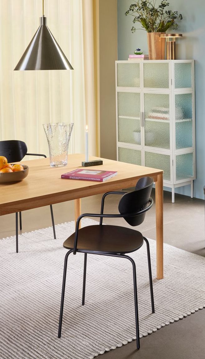 Holztisch mit einer schwarzen Stuhl und einem kleinen Hocker auf einem Teppich im Hintergrund.