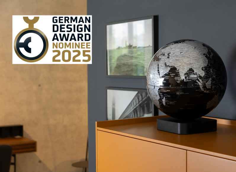 Schwarze Globus-Dekoration auf einem Tisch vor grauer Wand und Designpreis-Logo.