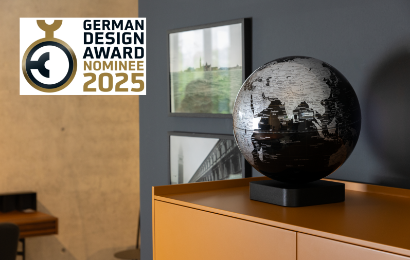 Schwarze Globus-Dekoration auf einem Tisch vor grauer Wand und Designpreis-Logo.