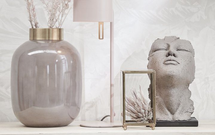 Vase mit Trockenblumen, Tischlampe, Skulptur und Bilderrahmen auf hellem Hintergrund.