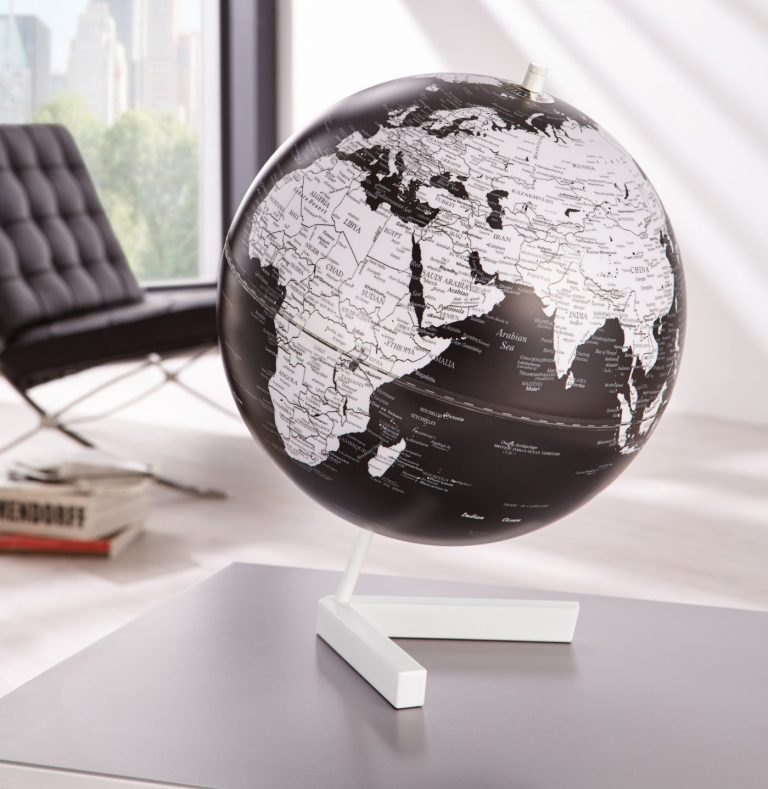 Schwarz-weißer Globus auf einem Tisch, im Hintergrund ein modern eingerichteter Raum.