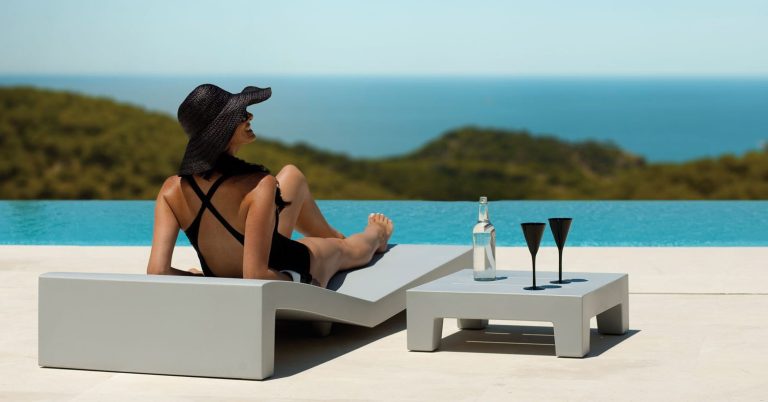 Frau in Badeanzug entspannt am Pool mit Blick auf das Meer, Getränke auf dem Tisch.