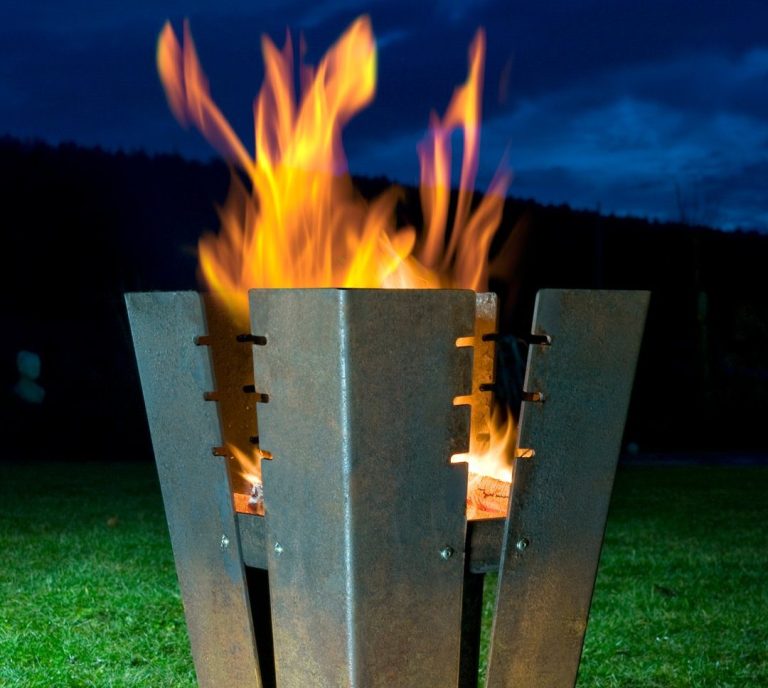 Feuer in einem modernen Feuerkorb bei Nacht mit dunklem Himmel im Hintergrund.