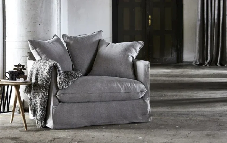 Grauer Sessel mit dekorativen Kissen, umgeben von minimalistischer Raumgestaltung.