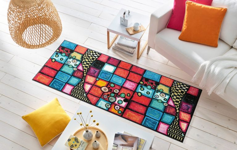 Bunter Teppich mit geometrischen Mustern und Blumen, umgeben von Kissen und einem Tisch.